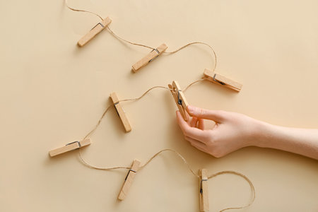Female hand with clothespins and rope on beige background