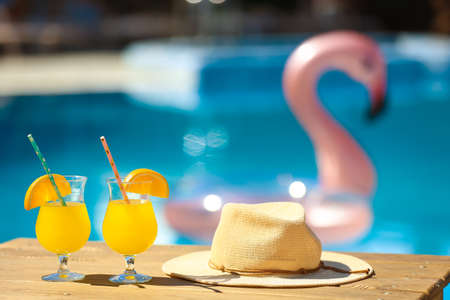 Glasses of cocktails and hats on table near swimming poolの写真素材