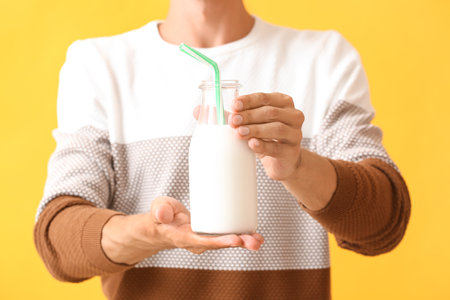 Young man with bottle of milk on color background, closeup
