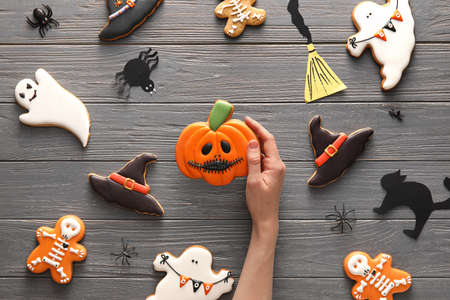 Female hand with tasty cookies for Halloween celebration on wooden backgroundの写真素材