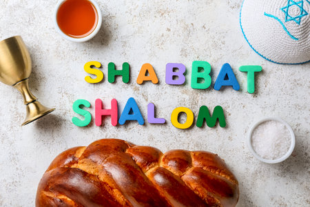 Text SHABBAT SHALOM with traditional challah bread, cup for wine and Jewish cap on grunge backgroundの写真素材