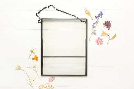 Composition with dried pressed flowers and empty frame on white wooden background