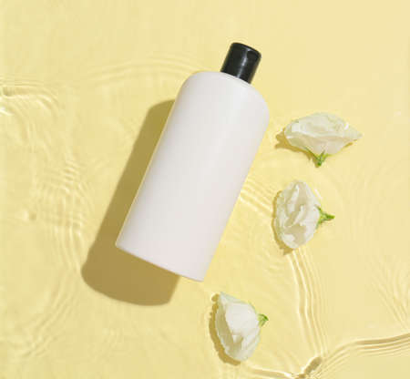 Bottle of shampoo and flowers in water on color background