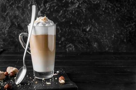 Glass cup of tasty latte with nuts on black background