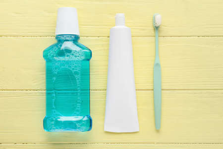 Tube with toothpaste, brush and mouthwash on color wooden background