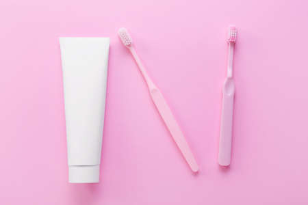 Tube with toothpaste and brushes on pink background