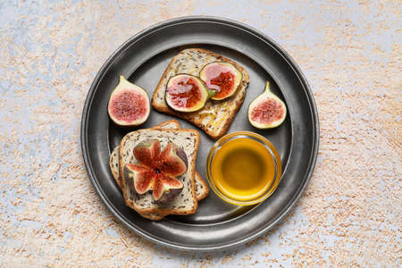 Toasts with ripe figs and honey on color background