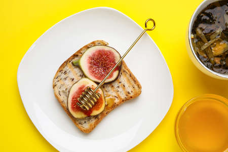 Toast with fresh ripe figs, honey and cup of tea on color backgroundの写真素材
