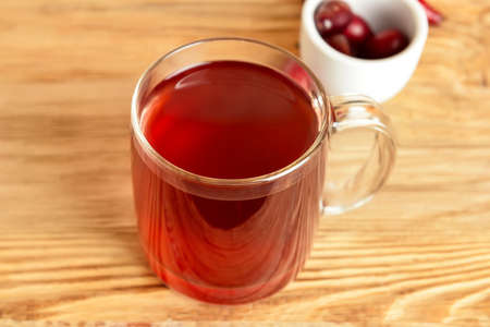 Glass cup of tasty dogwood drink on wooden background, closeup