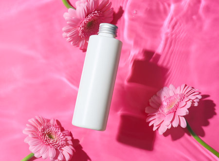 Bottle of cosmetic product and beautiful Gerbera flowers in water on color backgroundの写真素材
