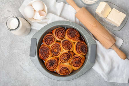 Baking dish with tasty cinnamon rolls on light background