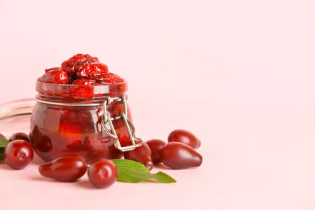 Jar of delicious dogwood jam and berries on pink background