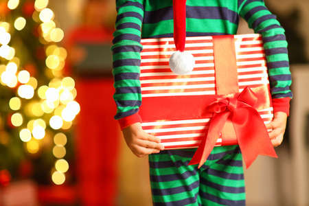 Little boy in Christmas costume holding gift at home, closeup
