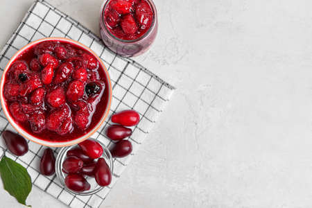 Composition with bowl of tasty dogwood jam and berries on light background