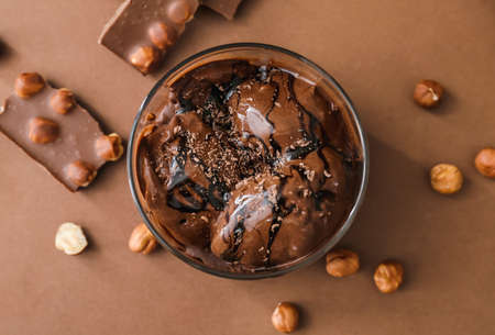 Bowl with delicious chocolate ice cream and hazelnuts on color background