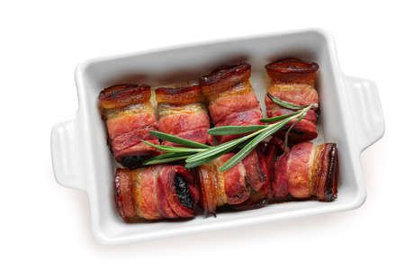 Baking dish with delicious prunes in crispy bacon on white backgroundの写真素材