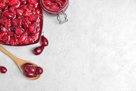 Bowl and jar of tasty dogwood jam on light background, closeup