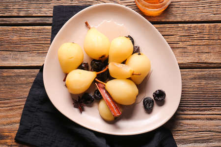 Dish with delicious poached pears, prunes, anise and cinnamon on wooden background