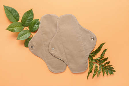 Reusable menstrual pads and green leaves on orange background