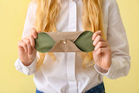 Woman with reusable menstrual pad on yellow background