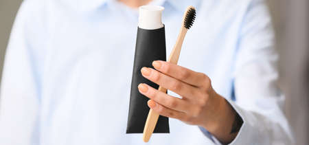 Woman with activated charcoal tooth paste and bamboo brush, closeup