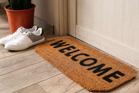Mat with word WELCOME and male sneakers near light wooden door in hall, closeupの写真素材