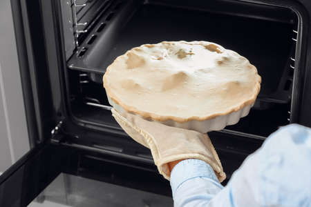 Woman putting uncooked chicken pot pie with vegetables in oven