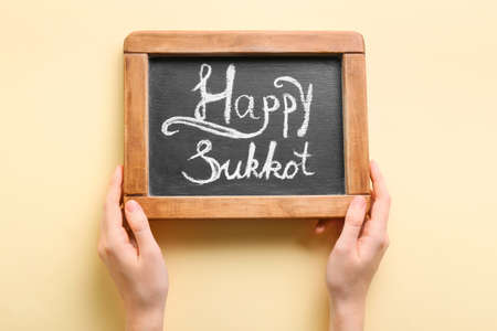 Hands holding chalkboard with text HAPPY SUKKOT on color backgroundの写真素材