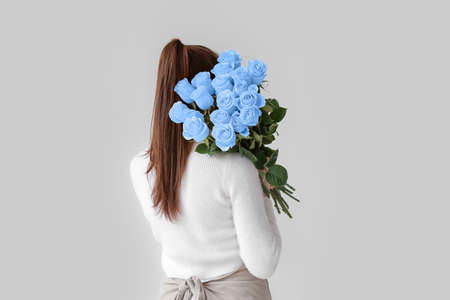 Woman with bouquet of beautiful blue roses on light backgroundの写真素材