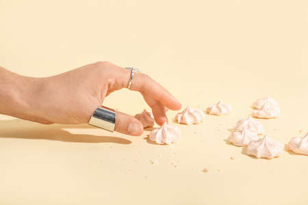 Female hand with sweet meringue on color background, closeup