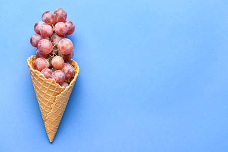 Wafer cone with tasty grapes on blue backgroundの写真素材