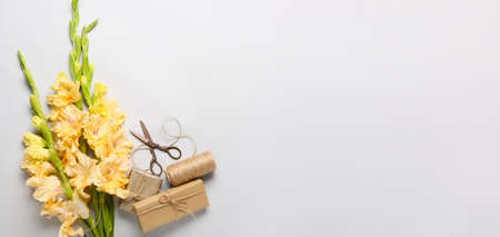 Beautiful gladiolus flowers, gift boxes, rope and scissors on light background with space for text,...
