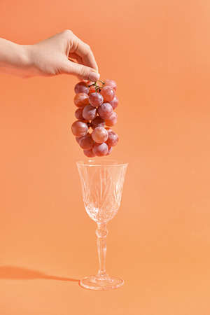 Woman holding fresh grapes and wine glass on color backgroundの写真素材
