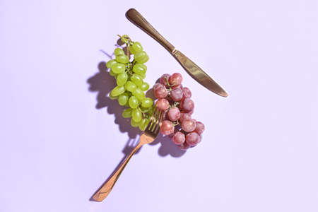 Tasty grapes and cutlery on light backgroundの写真素材