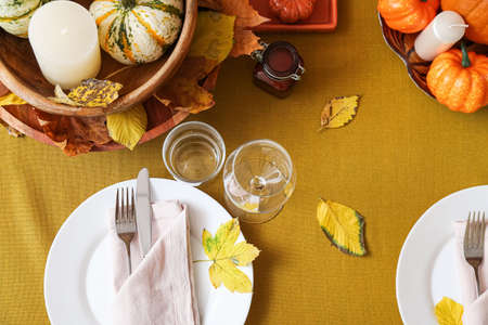 Beautiful table setting with fresh pumpkins and fallen leaves in roomの写真素材