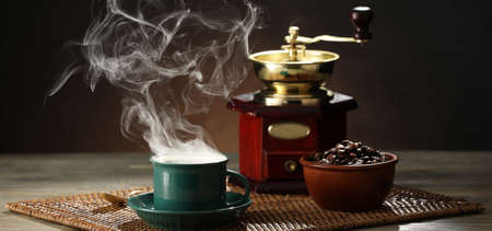 Cup of hot coffee, roasted beans and grinder on wooden tableの写真素材
