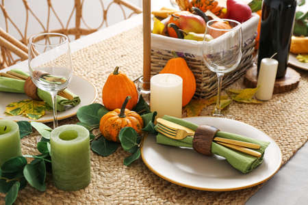 Beautiful table setting with fresh pumpkins and leaves in the room
