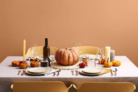 Autumn table setting with fresh pumpkins and candles near beige wall