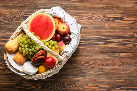 Wicker basket with tasty food for picnic on wooden backgroundの写真素材