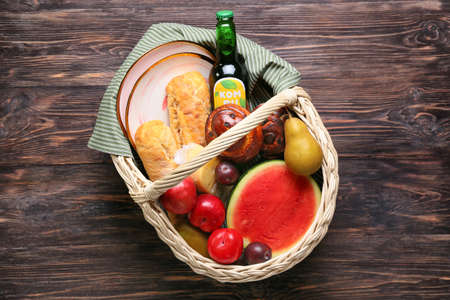 Wicker basket with tasty food and drink for picnic on wooden backgroundの写真素材