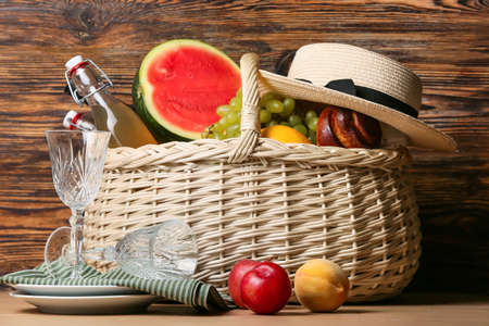 Wicker basket with tasty food, drink for picnic and tableware on wooden backgroundの写真素材