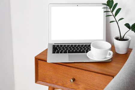 Laptop on wooden bedside table near light wall