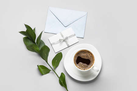Composition with cup of coffee, envelope, card and plant branch on gray backgroundの写真素材