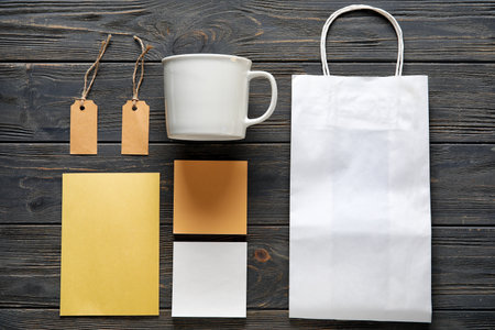 Composition with blank cup, paper bag, card and sticky notes on black wooden backgroundの写真素材