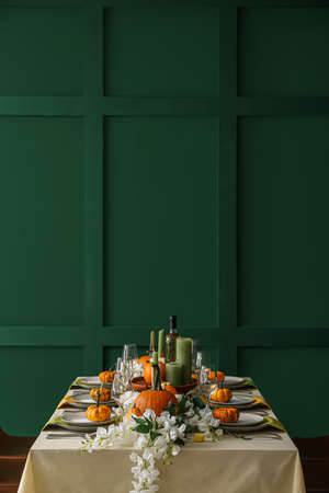 Autumn table setting with fresh pumpkins and flowers near green wall
