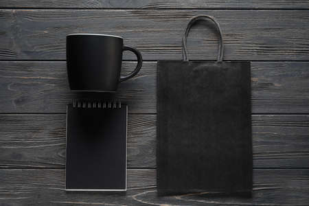 Blank cup, notebook and paper bag on dark wooden background