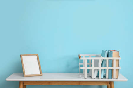 Basket with books and frame on table near blue wallの写真素材