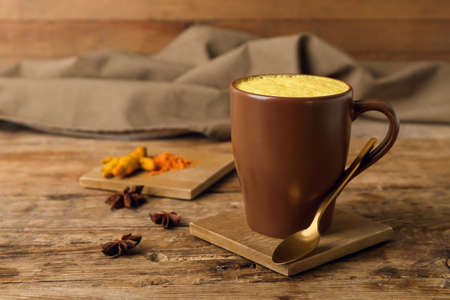 Cup of healthy turmeric latte with powder and star anise on wooden tableの写真素材