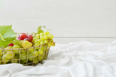 Basket with ripe grapes on white fabric
