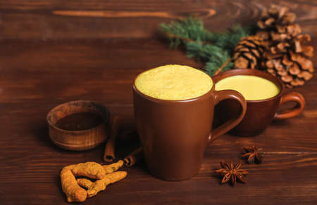 Cups of tasty turmeric latte with spices on wooden backgroundの写真素材